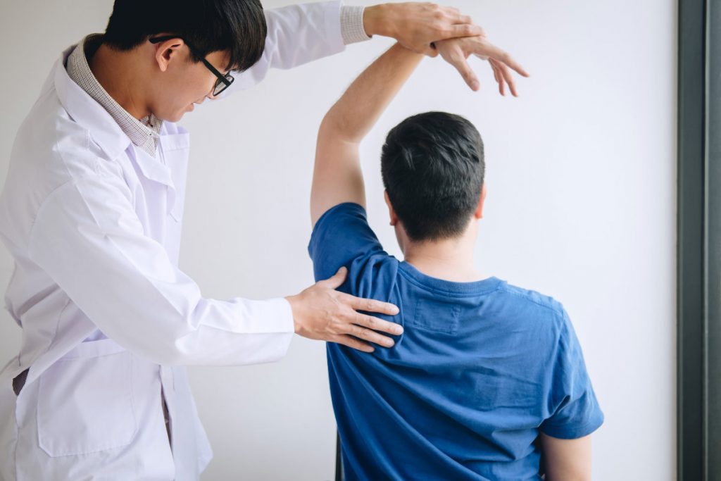 physiotherapist assisting a male patient while giving exercising treatment massaging the shoulder of patient in a physio room, rehabilitation physiotherapy