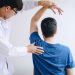 physiotherapist assisting a male patient while giving exercising treatment massaging the shoulder of patient in a physio room, rehabilitation physiotherapy
